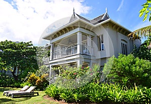 A large bungalow resort with sundeck chairs in front surrounded by green trees and plants