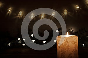 A large candle burns in the dark on a black background. Garland lights and stars. Christmas and New Year