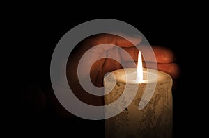 A large candle burns in the dark. On a wooden background.