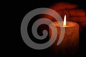 A large candle burns in the dark. On a wooden background.