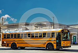 Large capacity yellow school bus from USA parked by building on bright day