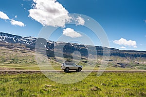 Large car parked on dirt road among the mountain and meadow on sunny day in summer
