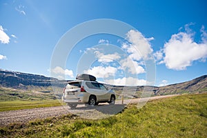 Large car parked on dirt road among the mountain and meadow on sunny day in summer