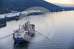 Large cargo ship sails along the river along the industrial zone leaving foamy trail