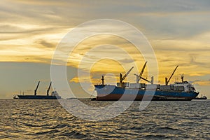 Large cargo ship for transportation import export goods anchor at sea in evening with golden sunset