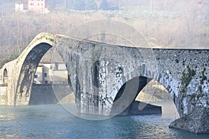 The large central arch of the Maddalena bridge built in stone, called the devil`s bridge, touched by the sun and wrapped in light