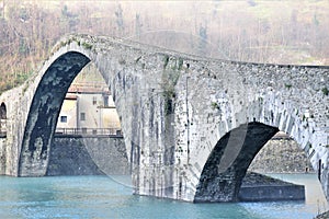 Large central arch of the Maddalena bridge built in stone under a fog cushion called the devil`s bridge on a cold winter morning.