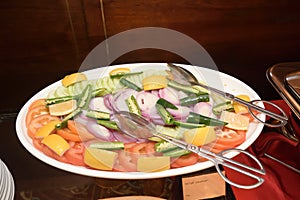 A large ceramic plate of salad dish with fork tongs laid out for serving