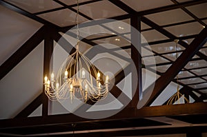 Large chandelier, light bulbs in the form of candles in formal restaurant hall with white walls and wooden beams