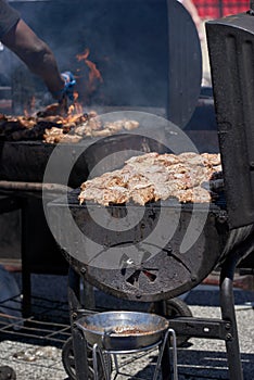 A large charcoal grill with of marinated chicken with a meat grill in the background.