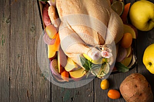 A large chicken stuffed with an apple with vegetables and fruits, top view