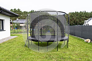 Large childrens jumping trampoline with protective net and closed zipper, standing in the garden, visible golden retriever dog.