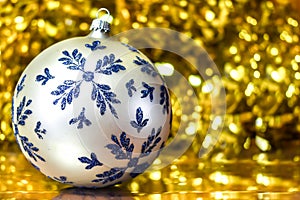 A large Christmas ball with blue snowflakes on a background of blurry defocused gold lights and tinsel. Christmas and New Years co