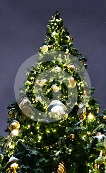 Large Christmas tree decorated with a garland and a large golden ball against the night sky