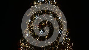 A large Christmas tree decorated with garlands, spinning in the square at night