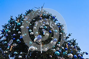 A large Christmas tree decorated with a star and round balls on a blue sky background.