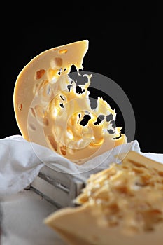 Large chunks of hard maasdam cheese on a black background. Cheese with lots of holes. Dutch Maasdamer cheese in a white wooden box
