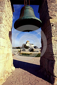 A large church bell and an Orthodox church with a golden dome