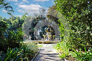 A large circular fountain with fish head sculptures in the garden surrounded by lush green trees at Huntington Library and Botanic