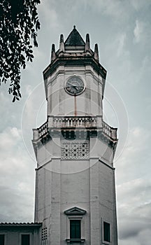 Large clock is affixed to the side of a tall tower on a backdrop of a cloudy sky