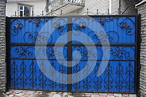 Large closed colored gates of iron black forged bars in a pattern on a blue metal wall