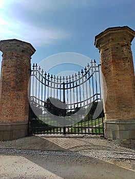 Large closed iron gate. Entrance to private property. In the background, a beautiful garden with trees. Elegant gate with arrow-