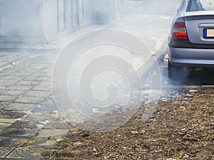 A large cloud of gray smoke from the exhaust pipe of a car in the courtyard of a residential building