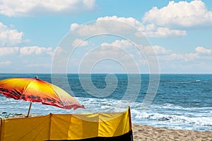 Large colorful beach parasol and windshield in the beach with a calm view to the Atlantic ocean.