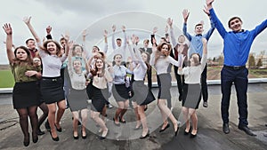 A large company of students on the roof of their school cheerfully bounce while taking a photo