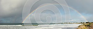 large complete full half circle rainbow stretching across the sky into the ocean at Apollo Bay, Victoria, Australia