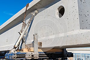 A large concrete beam secured by a hydraulic mechanism and chains to a car platform