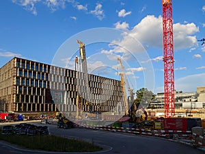 Large construction site with crane cement mixers next to modern industrial building. Sunny summer day, blue sky, no people