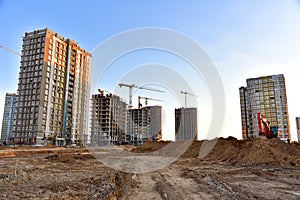 Large construction site with tower cranes and buildings on sunset background. Excavator during Road work and excavation for laying