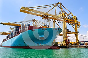 Large container cargo ship next to the cranes in the process of loading and unloading goods