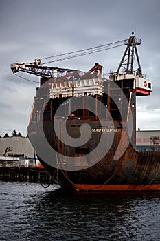 A large container ship is docked at Seaspan, named `Seaspan Survivor`. Cranes are atop this old, rusty ship and large anchor chai