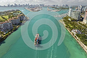 Large container ship entering in Miami harbor main channel near South Beach. Luxurious hotels and apartment buildings on