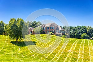 Large country brick house and summer landscape with a perfect lawn. Blue sky and white clouds