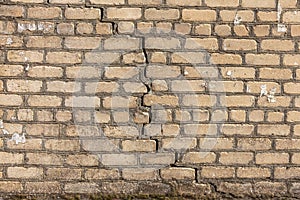 A large crack in the old stone wall. Background of a stone brick wall of a building with a deep through dangerous crack. Ruined
