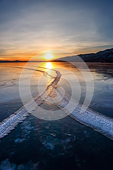 Large cracks in the clear smooth blue ice of Lake Baikal at sunset. Siberia Russia