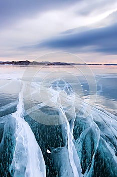 Large cracks in the clear smooth blue ice of Lake Baikal at sunset. Siberia Russia