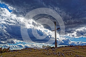 Large cross on rugged hill against blue sky by dramatic clouds photo