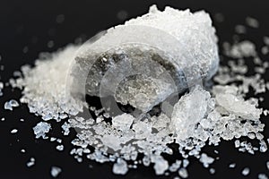 Large crystal of salt on black reflective surface; selective focus; natural edible salt