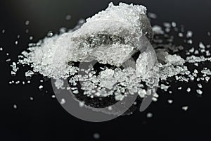 Large crystal of salt on black reflective surface; selective focus; natural edible salt