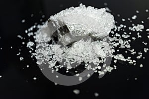 Large crystal of salt on black reflective surface; selective focus; natural edible salt