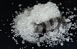 Large crystal of salt on black reflective surface; selective focus; natural edible salt