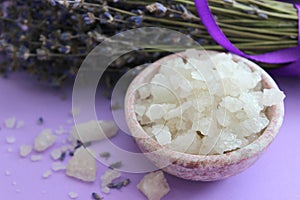 Large crystals of sea salt and lavender flowers, close-up on a purple background.