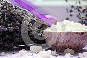 Large crystals of sea salt and lavender flowers, close-up on a purple background.