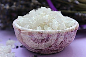 Large crystals of sea salt and lavender flowers, close-up on a purple background.