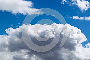 A large Cumulus cloud in the blue sky. In the top left corner flies a little gull.