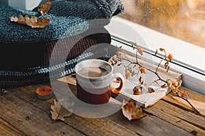 Large Cup of cappuccino on vintage brown background. Autumn, fall leaves, hot steaming cup of coffee and a warm scarf on wooden ta